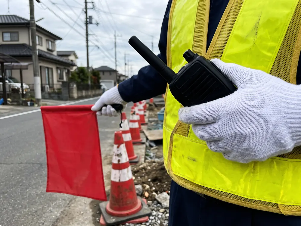 無線機と赤い旗を持つ手と、並べたコーン
