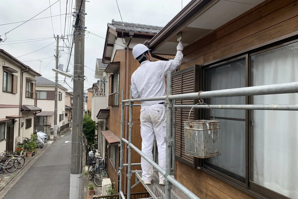 足場の上で軒を塗る職人の後ろ姿