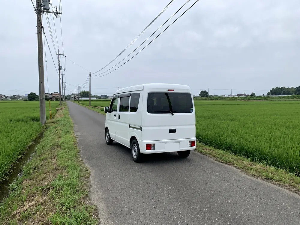 田んぼの間の道を走る白い軽自動車