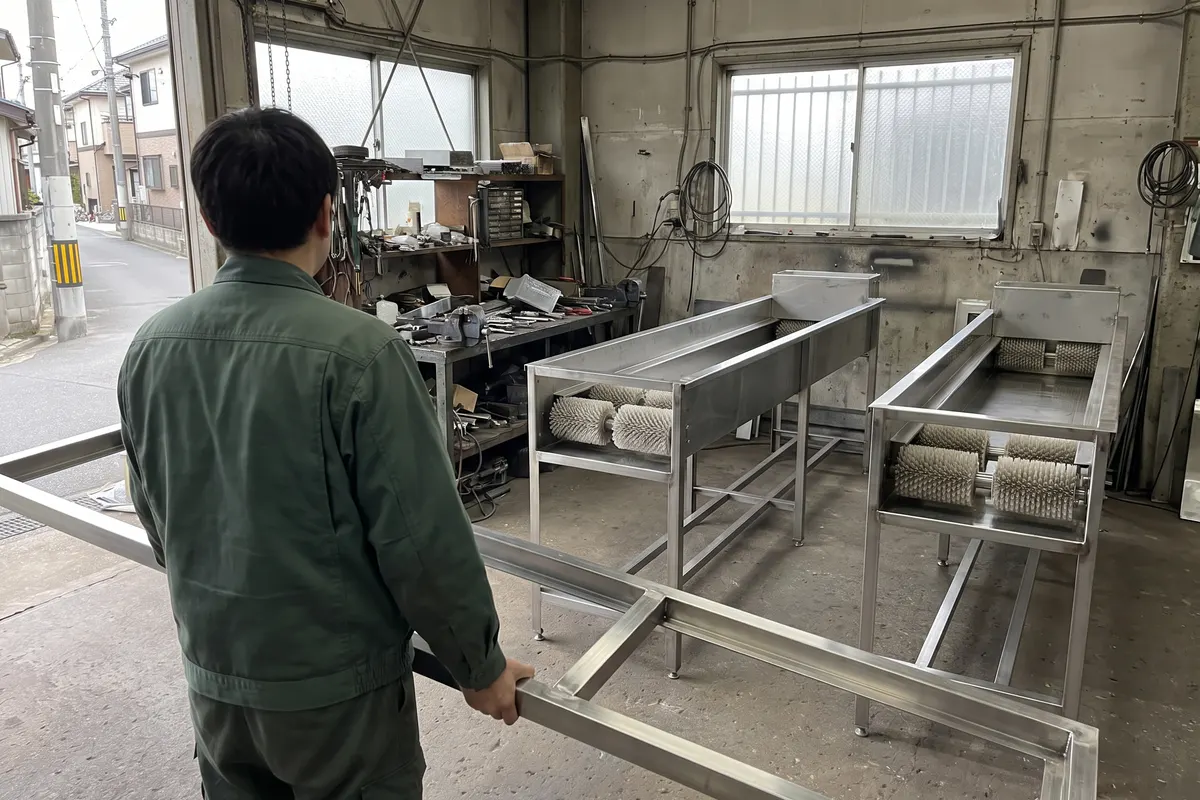 機械の部品を運ぶ作業員の後ろ姿