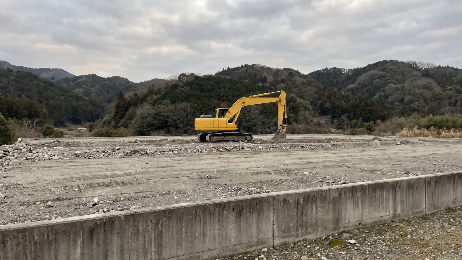 山あいの処分場の埋立地と重機。手前にコンクリートの擁壁