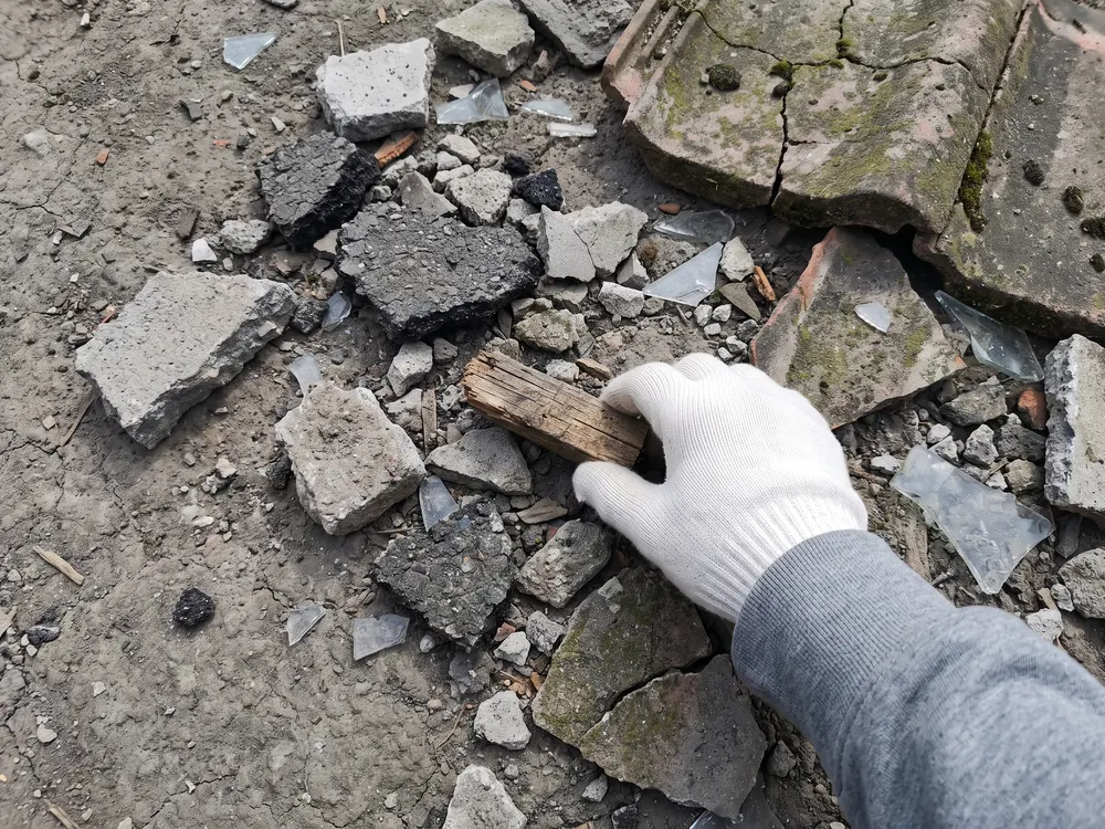 地面に広げたがれきから、混じっていた木片を手袋の手で拾い出す様子